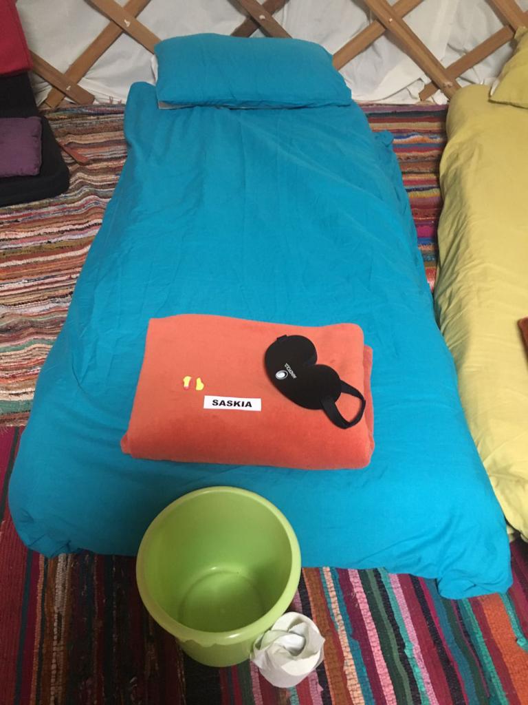 A bed, blankets, sleeping mask, ear plugs, bucket and toilet roll at an ayahuasca retreat in East Anglia.